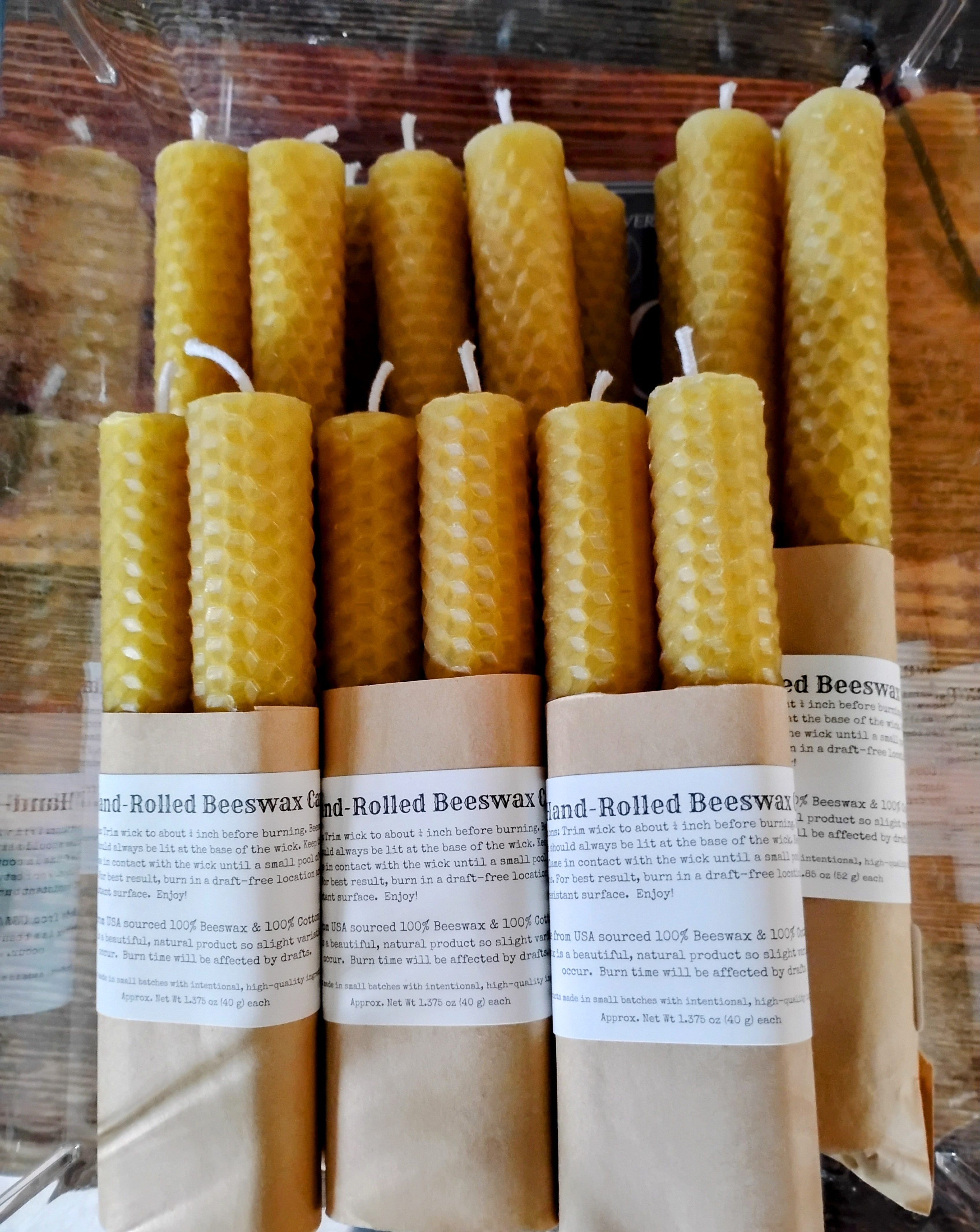 A set of yellow honeycomb beeswax taper candles wrapped in brown kraft paper labels, packaged in a clear plastic sleeve on a wooden surface.